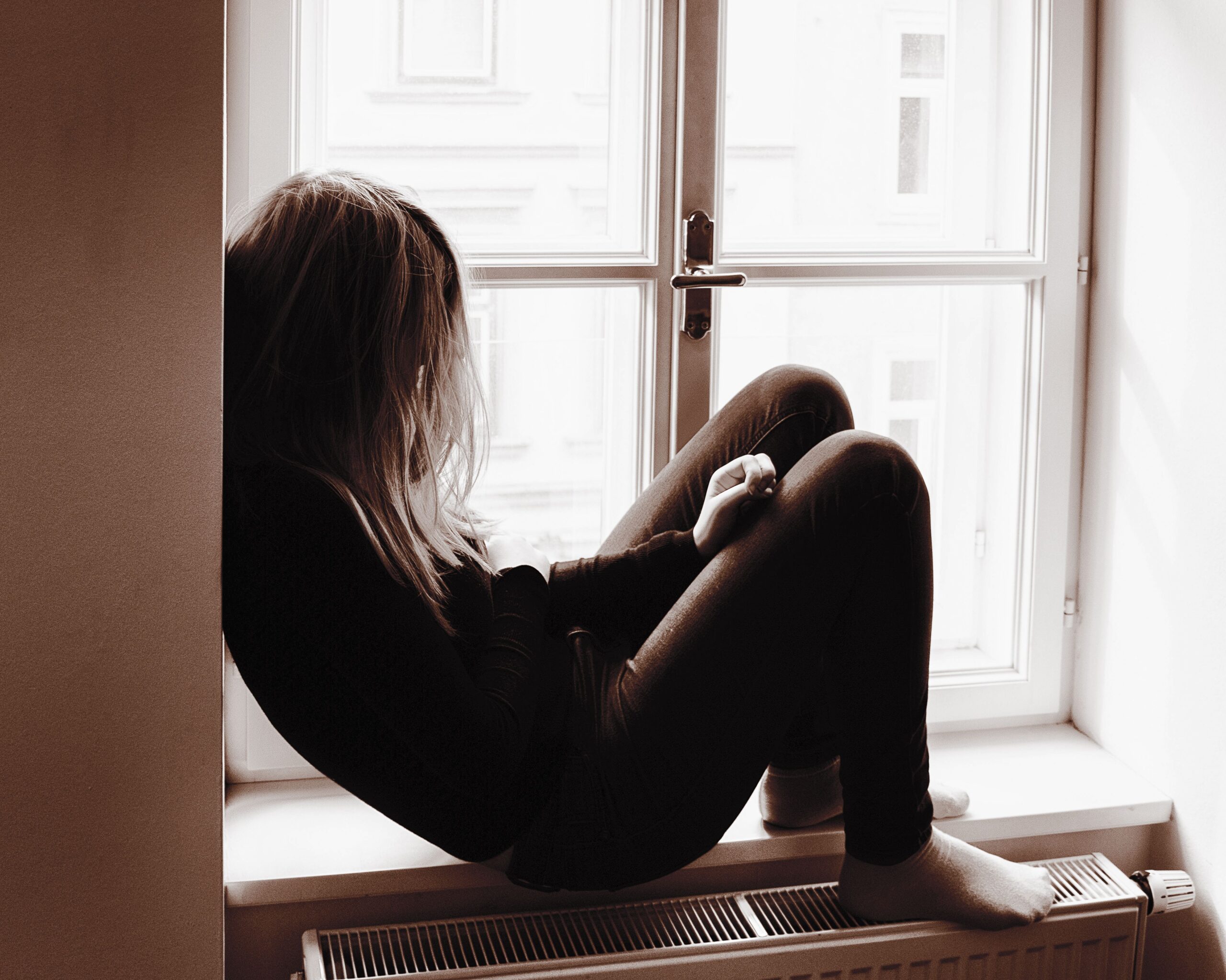 Girl sitting next to window feeling lonely and stressed